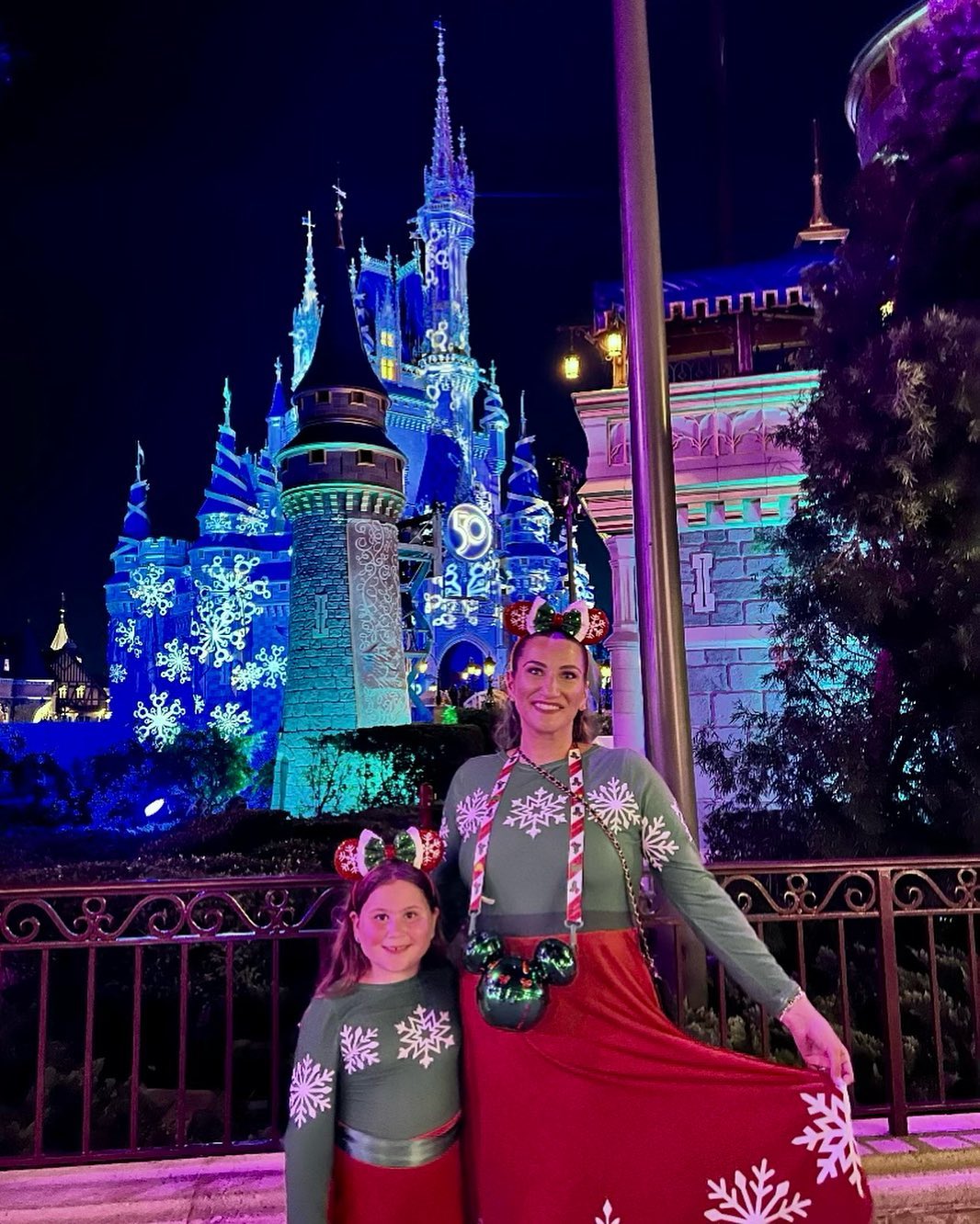 Two models stand in front of a decorated Cinderella Castle at Disneyworld in their red and green Very Merry Christmas dresses, the perfect way to dress like a holiday Minnie to get into the party spirit. 